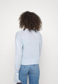 Helles blaues Strickpullover mit lockerer Passform, geripptem Saum und übergroßen Ärmeln, kombiniert mit blauen Jeans. Strukturiertes Material.