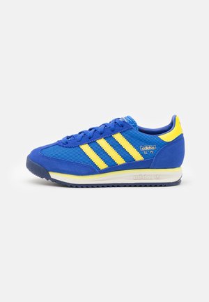 Baskets Adidas SL 72 bleues avec des bandes jaunes, languette jaune au talon et semelle blanche avec le logo Adidas sur le côté.