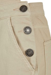 Beige stoffbukser med cargo-stil, dekorative metalldekorasjoner, en sidelomme og synlige sømmer. Glatt tekstur med en tettsittende passform.