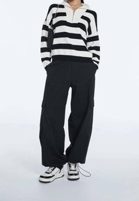 Sweater noir et blanc à rayures avec demi-zip, associé à un pantalon cargo noir ample et des baskets noires et blanches imposantes. Maille texturée et matériau robuste.