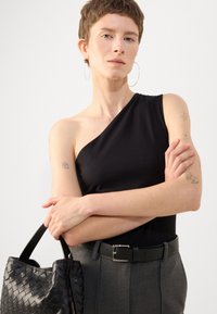 Bodysuit negro de un solo hombro combinado con pantalones grises a medida. Los accesorios incluyen un bolso de mano negro trenzado y grandes pendientes de aro.