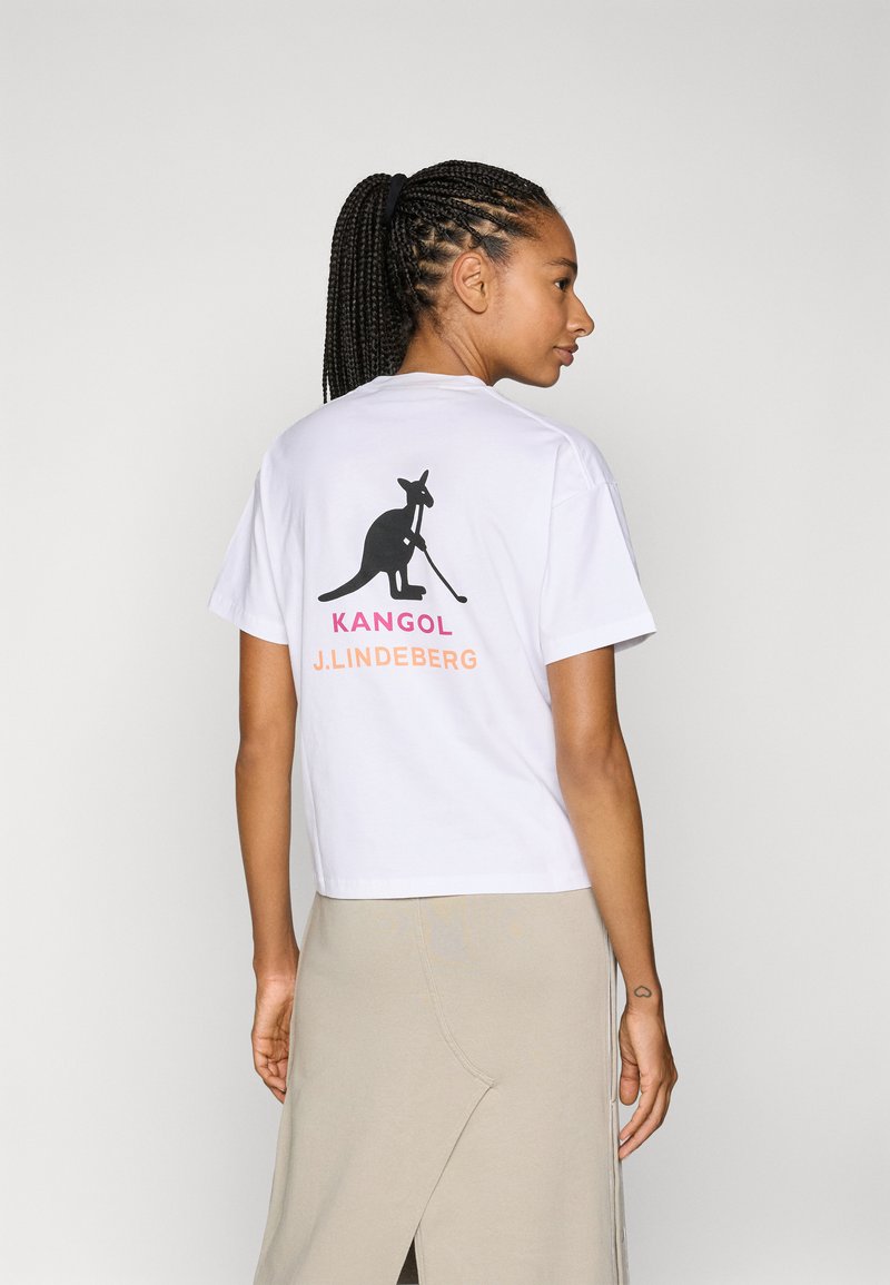 Valge lühikeste varrukatega T-särk, millel on must kenguru graafika ja "KANGOL J.LINDEBERG" tekst roosa ja oranži värviga seljal.