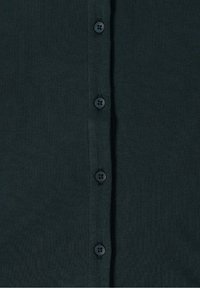 Tissu tricoté vert foncé avec une rangée verticale de cinq boutons noirs cousus sur une patte.