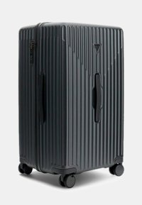 Zwarte harde koffer met verticale ribbelstructuur, boven- en zijhandvatten, een combinatieslot en vier soepel rollende wielen.