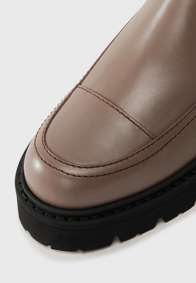 Stivaletto in pelle marrone con punta arrotondata, dettagli di cucitura discreti e una spessa suola in gomma nera per la trazione. Texture complessivamente liscia.