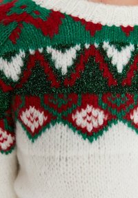 Strickpullover mit einem weißen Körper und einem gemusterten Schulterbereich in Grün, Rot und Weiß, akzentuiert mit metallischen grünen Fasern und Herzmotiven.