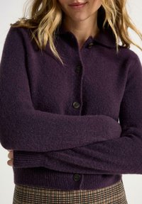 Mörklila stickad cardigan med en texturerad yta, med en krage och två svarta knappar framtill.