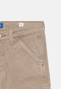 Μπεζ βαμβακερό παντελόνι με μπροστινή τσέπη, θηλιά για ζώνη, ασημένιο κουμπί και ετικέτα μεγέθους "128" ορατή μέσα στη μέση της μέσης.