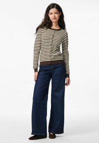 Pruhovaný cardigan v béžové a hnědé barvě, s dlouhými rukávy, s knoflíkovou přední částí, kombinovaný s širokými tmavě modrými džíny a tmavými botami. Hladká pletená textura.