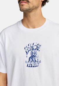 White cotton t-shirt featuring a blue graphic design of a skull with a hat and text, displayed prominently at the center.