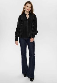 Black blouse with vertical silver stripes, long puff sleeves, and a small collar, paired with dark flared jeans and black ankle boots.