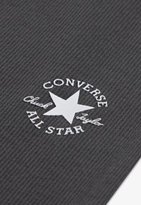 Γκρι ύφασμα με ανάγλυφη υφή ραφής και λευκό κεντημένο λογότυπο ενός αστεριού, το κείμενο «CONVERSE» και «ALL STAR» σε κυκλικό σχέδιο.