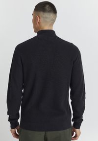 Pulover tricotat închis cu guler înalt, textură ribbed și mâneci lungi. Croiala este ajustată pe talie, prezentând un design curat și simplu într-o nuanță uni.