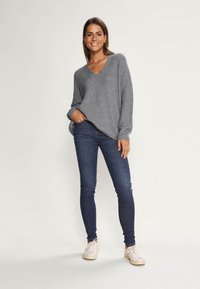Maglione grigio oversize a scollatura a V con texture a coste. Abbinato a jeans skinny blu scuro e sneakers chiare. Outfit semplice e casual.