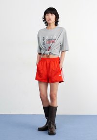 Grijze t-shirt met een knoop in de taille, rode gestreepte shorts met witte zijkanten, en kniehoge zwarte leren laarzen.