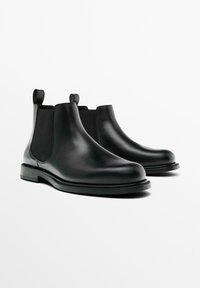 Schwarze Leder Chelsea-Boots mit elastischen Seiteneinsätzen, Zuglaschen an der Rückseite und flachen, niedrigen Absätzen auf einem weißen Hintergrund.