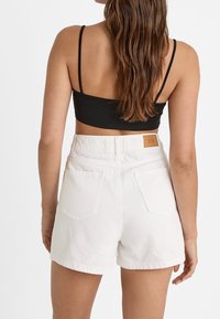 Shorts in denim bianco con vita alta, dotati di tasche posteriori e un piccolo etichetta marrone in vita. Top nero con spalline sottili.