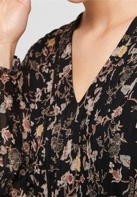 Blusa nera a fiori con scollatura a V, maniche lunghe e texture plissettata. I motivi floreali in rosa, blu e giallo accentuano il design.