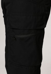 Un pantalon cargo noir en tissu résistant présentant de multiples poches, y compris une poche zippée, et une finition texturée.