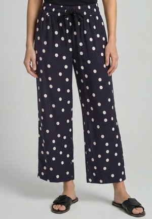 Marineblaue weit geschnittene Hose mit weißen Punkten, einem elastischen Bund mit schwarzem Kordelzug, getragen mit schwarzen Slip-On-Sandalen.