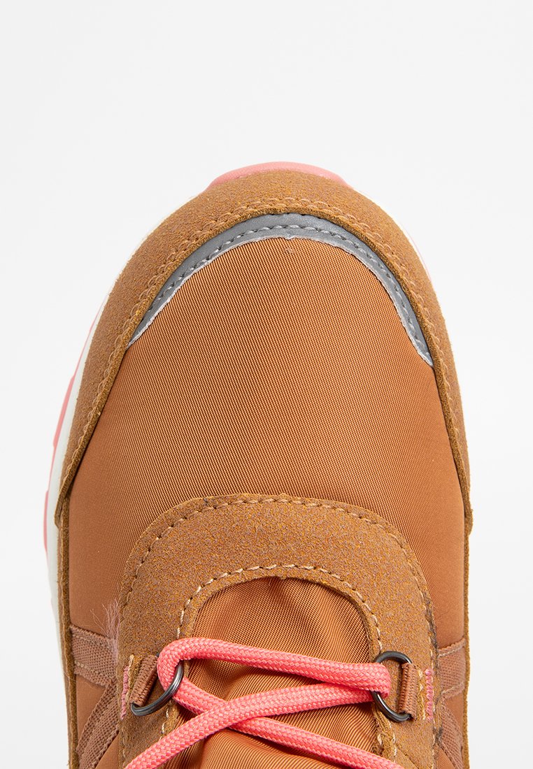 Ansicht von oben auf einen braunen Sneaker mit Wildleder- und Stoffpaneelen, der pinke Schnürsenkel und einen reflektierenden Streifen in der Nähe der Zehen hat.