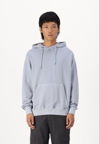 Lys grå hættejakke med snore, frontlomme og ribbede ærmer. Stoffet ser blødt ud med en afslappet pasform og minimal udsmykning.