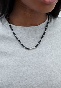 Must have tumehel, millel on hõbedased aksendid, kantud heledast hallist särgist, näidates mati ja poleeritud tekstuuri segu.