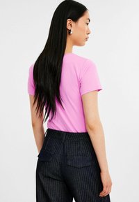 Korte mouwen, roze katoenen t-shirt met ronde hals, gecombineerd met donkere pinstripe jeans met achterzakken, een gladde textuur en een getailleerd ontwerp.