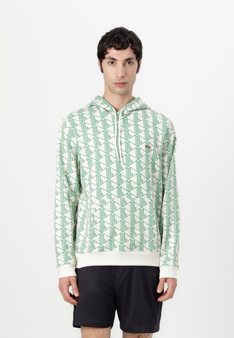 Felpa con cappuccio realizzata in tessuto morbido, caratterizzata da una base bianca con motivi geometrici verdi. Include una tasca frontale e polsini a coste.