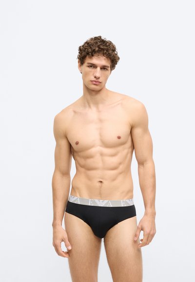Fekete férfi alsónadrágok szürke elasztikus derékpánttal, amelyen logó látható. Az anyag simának és testhez állónak tűnik, kiemelve a test formáját.