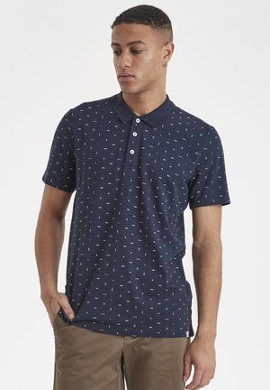 Navy polo shirt with a small white geometric pattern, three-button placket, and a classic collar. Soft texture, short sleeves, casual fit.