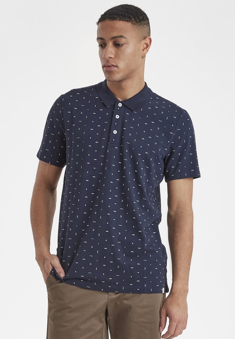 Marineblaues Poloshirt mit kleinem weißen geometrischen Muster, drei Knöpfen Knopfleiste und klassischem Kragen. Weicher Textur, kurze Ärmel, lässige Passform.