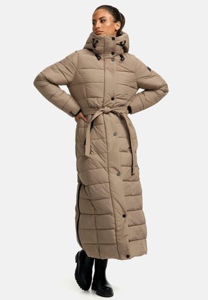 Long, beige puffer coat with a high collar, tied waist, quilter pattern, snap buttons, and side slits. Styled with black boots.
