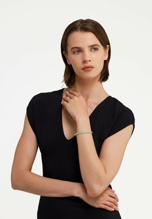 Black short-sleeve dress with a V-neckline, featuring a textured fabric. A light green bracelet adorns the wrist. Neutral background.
