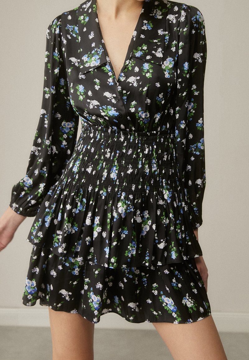 Robe noire à manches longues avec imprimé floral bleu et blanc, décolleté en V profond, taille élastiquée et jupe à volants à étages.