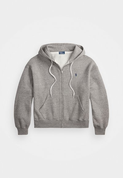 Grå hettegenser med glidelås som har hvit fôr, frontlommer og en blå logo på venstre bryst. Snorene på hetten kan justeres.