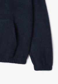 Giacca in pile blu navy con maniche e tasca laterale, con polsini e orlo elasticizzati, presentata su sfondo bianco.