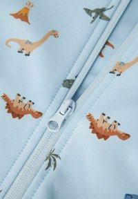 Hellblauem Stoff mit kleinen Dinosaurier- und Vulkanillustrationen in verschiedenen Farben, mit einem zentralen weißen Reißverschluss und strukturierten Details.