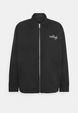Chaqueta ligera negra con cierre frontal de cremallera. Presenta un cuello puntiagudo y bolsillos laterales. Logo bordado "Wild Peach" en el pecho.