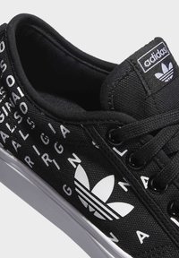 Svart canvas sneakers med vit text och logodesign, runda skosnören och en gummisula som accentueras av en vit kant.