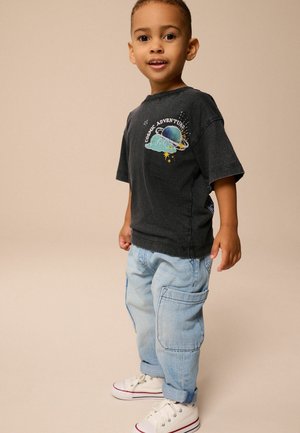 Camiseta de algodón gris con gráfico de "Aventura Cósmica", combinada con pantalones cargo de color azul claro y zapatillas blancas. Diseño de outfit casual sencillo.