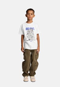 Biała koszulka z krótkim rękawem z graficznym nadrukiem w niebieskim i czarnym kolorze. Połączona z oliwkowymi spodniami cargo i beżowymi sneakersami z niebieskimi akcentami.