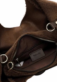 Brown handbag with soft, textured outer material, zippered interior, metal hardware, and a dark fabric lining. Features a brand tag.