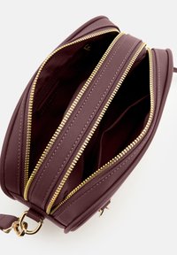 Runde, burgunderfarbene Handtasche aus strukturiertem Leder, ausgestattet mit goldfarbenen Reißverschlüssen und mehreren Fächern zur Organisation.