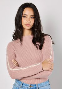 Rosa gerippter Pullover mit langen Ärmeln, der eine cremefarbene Naht entlang der Arme aufweist. Leichter Stoff, runder Ausschnitt und figurbetontes Design.