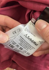 Burgundy garment label from Schöffel displaying care instructions. Materials are soft, with a woven texture and a smooth finish.