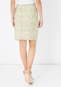 Falda verde con un diseño texturizado, de longitud a la cadera, que presenta un corte ajustado y una cinturilla plana, combinada con sandalias de tacón de color claro.