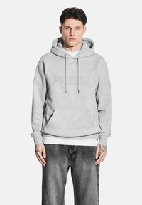 Szara bluza z kapturem i troczkami, z dużym, tonowym logo "PROSTO". Połączona z czarnymi, zwężającymi się dżinsami, które mają luźny krój.