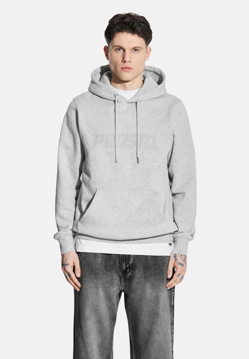 Szara bluza z kapturem i troczkami, z dużym, tonowym logo "PROSTO". Połączona z czarnymi, zwężającymi się dżinsami, które mają luźny krój.