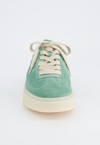 Sneaker verde in suede con lacci crema, punta arrotondata, suola in gomma e cuciture lungo il corpo e la suola.